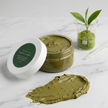 Green Tea Matcha beauty mask with open jar, and plant on marble surface